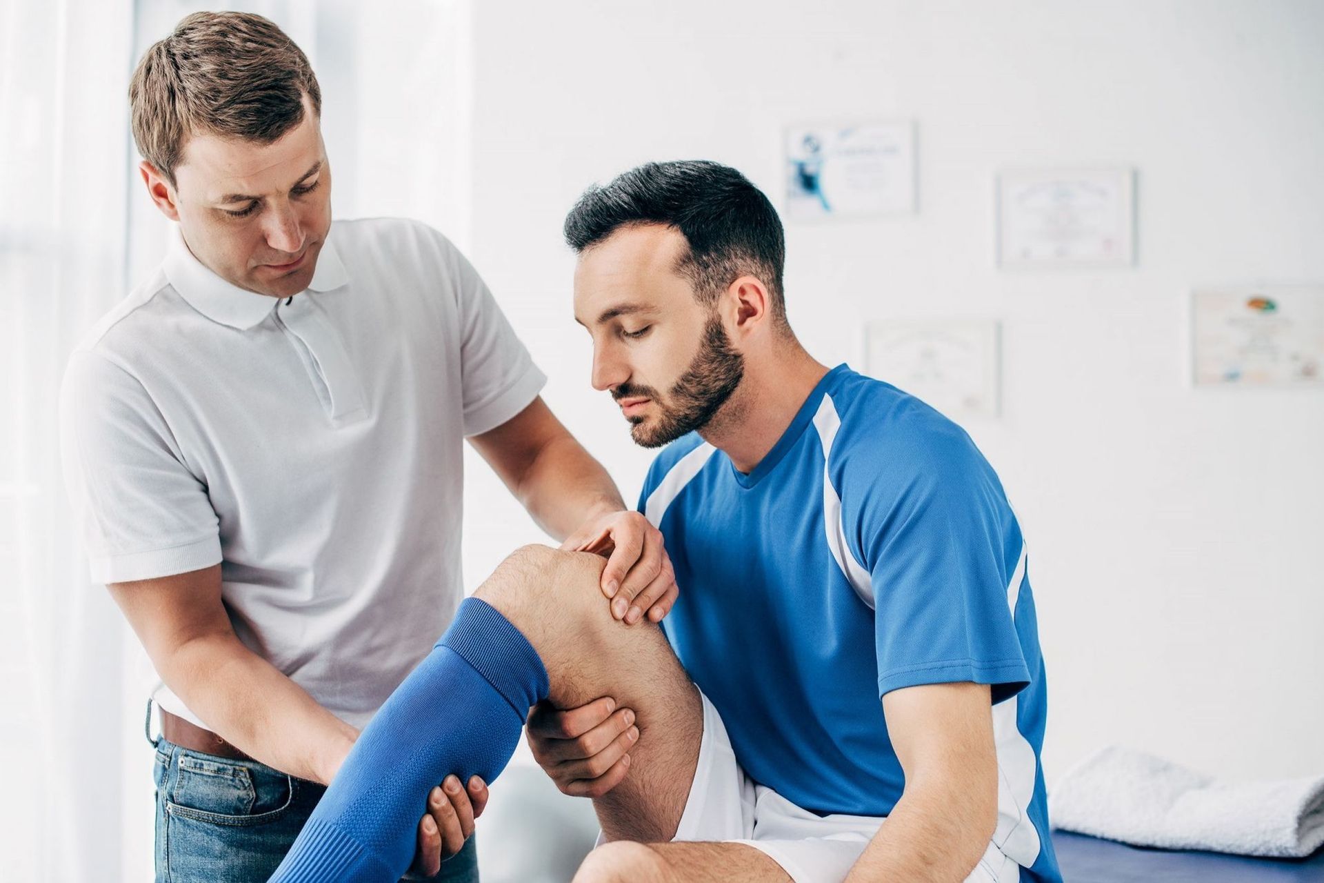 Ein Sporttherapeut untersucht das Knie eines männlichen Sportlers in einer Klinik, die sich auf die Beurteilung von Verletzungen und die Rehabilitation konzentriert.